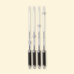 Lot de quatre brochettes longues en inox avec manche noir et bagues réglables, alignées sur fond beige.