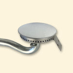 Brûleur en acier pour plancha gaz Vivaplancha, avec tête ronde perforée et tube courbé, présenté sur fond beige.