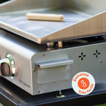 Nahaufnahme der Vivaplancha-Plancha mit dem Fettauffangbehälter aus Edelstahl und einem Reinigungswerkzeug auf der Platte, versehen mit einem Abzeichen „Sehr einfache Pflege“.